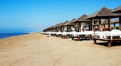 Strandansicht in Antalya, Türkei, mit einer Reihe von luxuriösen Cabanas und Liegen, die sich entlang des Sandstrandes erstrecken, mit dem Meer am Horizont.