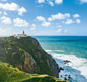 Steilküste in Portugal. Auf der Klippe steht ein Leuchtturm. Am fuß schäumt das Meer