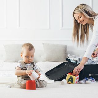 Frau packt koffer und Baby sitzt davor auf dem Bett
