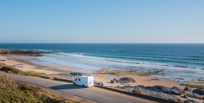 Eine Reihe von Wohnwagen und Wohnmobilen sind auf einem Campingplatz, Costa do Vizir Camping, nahe der Küste geparkt, umgeben von Bäumen und grünen Flächen.