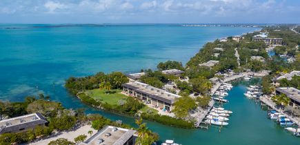 Blick auf Buttonwood Bay auf Key Largo. Einige Häuser auf kleinen Inselchen, davor kleine Boote, Meer und Palmen. Blauer Himmel.