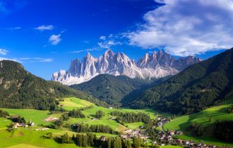Malerisches Tal in der Steiermark mit grünen Wiesen und bewaldeten Hängen, umgeben von majestätischen Bergen.