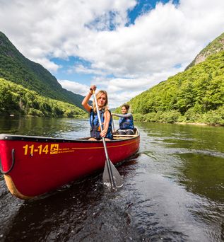 Kanufahrer in einem roten Kanu auf einem Fluss in der Region Quebec umgeben von bewaldeten Felsen