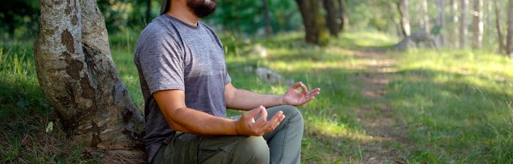Ein Mann meditiert im Wald. Bei dieser Praxis, die manchmal auch als „Waldbaden“ oder Waldmeditation bezeichnet wird, geht es darum, sich mit der Natur zu verbinden, um Ruhe zu finden, Stress abzubauen und die Achtsamkeit zu steigern.