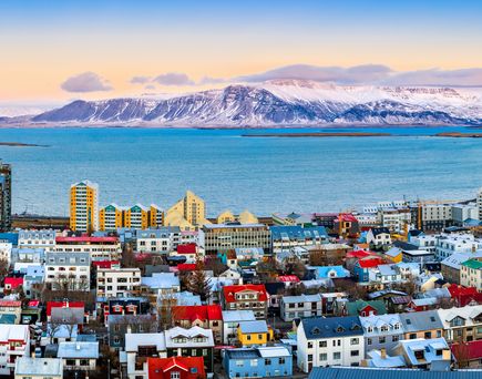 Blick über die farbenfrohen Häuser Reykjaviks, davor Wasser, davor die schneebedeckten Berge.