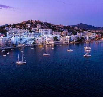Blick auf den kleinen Hafen von Costa Calma. Einige Botte im Wasser, kleiner Strandabschnitt und dahinter Hotels und Gebäude.
