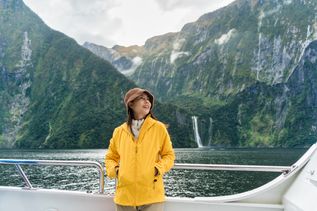 Frau im gelben Regenmantel an der Reeling eines Kreuzfahrtschiffes in einem Fjord