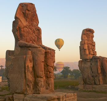 Die zwei kolossalen Statuen der Memnonkolosse, die majestätisch in der Landschaft stehen und die Überreste eines antiken Tempels markieren.