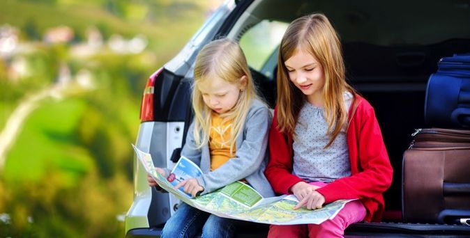 Zwei Kinder blicken interessiert auf eine Karte im Kofferraum eines Autos.