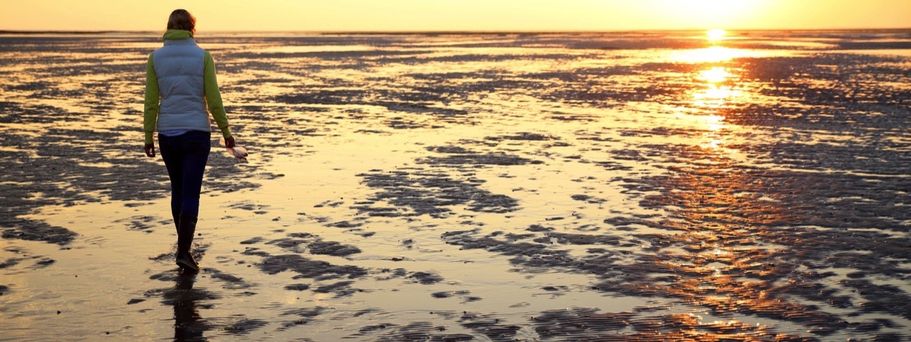 Eine Person geht auf einem Strandweg bei Sonnenuntergang.