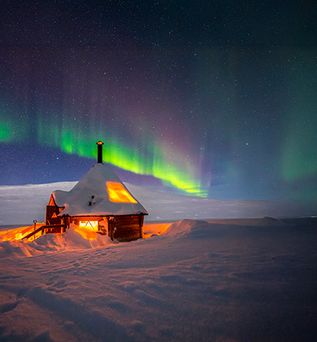 Hütte im Schnee in Finnland, im Hintergrund Polarlichter