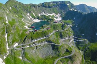 Luftaufnahme des Kessels des Balea-Sees, des steilen Fagaras-Gebirges und der Transfagarasan-Straße, die sich entlang der felsigen Klippen der Berge schlängelt. Karpaten, Rumänien