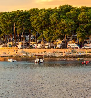 Blick vom Wasser auf Strand und Campingplatz in Istrien. Wald dahinter zu sehen.