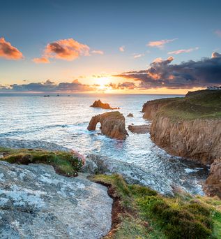 Eine Küstenlandschaft in Cornwall, England, mit einer Bucht und Felsen bei Sonnenuntergang.