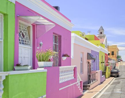 Eine enge, gepflasterte Straße im Bo-Kaap-Viertel in Kapstadt, Südafrika, gesäumt von Reihen leuchtend bunter Häuser.