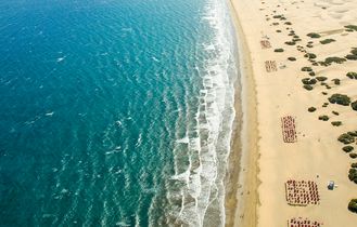Ein Sandstrand mit türkisfarbenem Wasser, umgeben von Gebäuden.