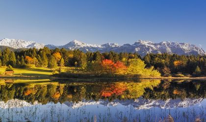 Eine Landschaft mit einem See, der sich in den Bergen spiegelt, und Bäumen in Herbstfarben.