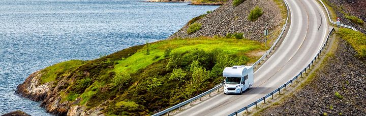Eine kurvenreiche Küstenstraße in Norwegen schlängelt sich entlang eines Fjords, umgeben von Bergen.