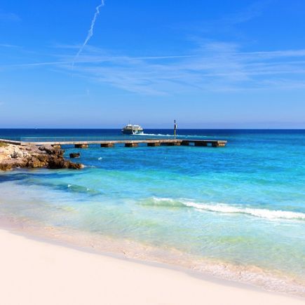 Ein Sandstrand mit türkisblauem Wasser und einem bewölkten Himmel.