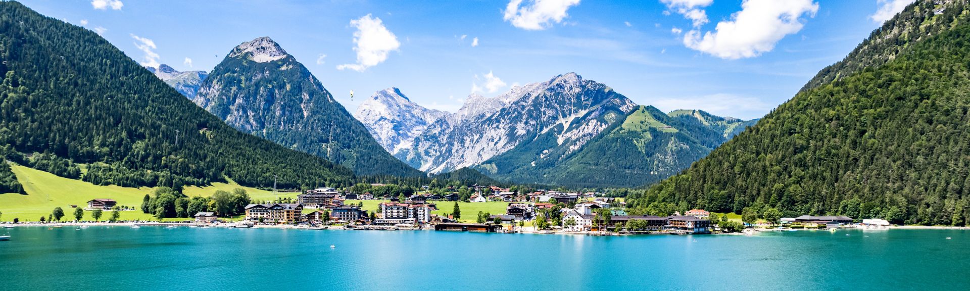 Achensee in Österreich. Im Vordergrund ein Segelbötchen, dahinter Berge und blauer Himmel.
