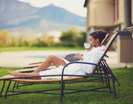  Eine Frau entspannt sich auf einer Chaiselongue auf einer Terrasse mit Blick auf das Meer bei Sonnenuntergang.