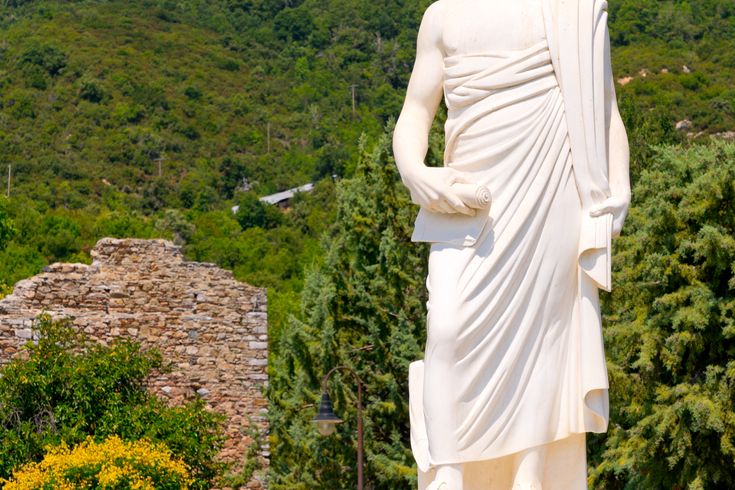 Weiße große Statue vor kleiner Gedenkstätte und Wald im Hintergrund.