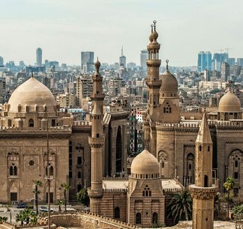 Eine Panoramansicht der Zitadelle von Kairo, mit mehreren großen Moscheen und Minaretten, die sich vor der modernen Skyline der Stadt abzeichnen.