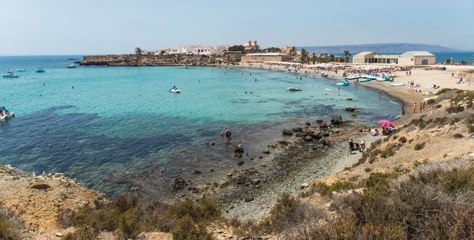 Eine Küstenlandschaft mit einem Sandstrand und türkisfarbenem Wasser.