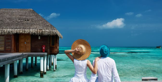 Ein Paar sitzt auf einem Steg und blickt auf die Überwasser-Bungalows.