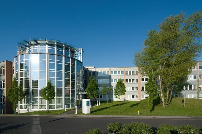 Modernes Bürogebäude mit Glasfassade und gepflegter Grünanlage unter klarem, blauem Himmel.