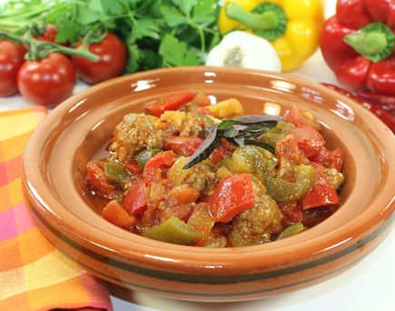typisch tunesisches Gemüsegericht in rundem, braunem, tiefen Teller. Auf bunter Tischdecke, Tomate und Paprika im Hintergrund