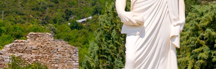 Weiße große Statue vor kleiner Gedenkstätte und Wald im Hintergrund.