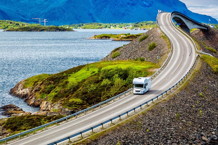 Eine kurvenreiche Küstenstraße in Norwegen schlängelt sich entlang eines Fjords, umgeben von Bergen.