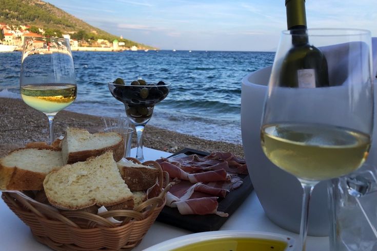 Ein Glas Weißwein und eine Platte mit Schinken am Meer.