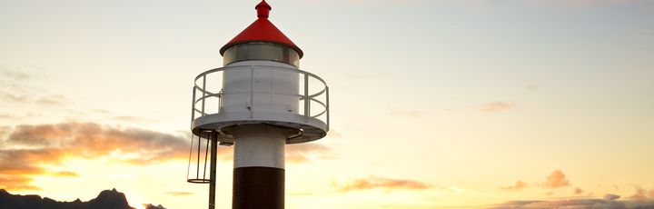 Ein rot-weißer Leuchtturm steht auf einer felsigen Küste bei Sonnenuntergang.