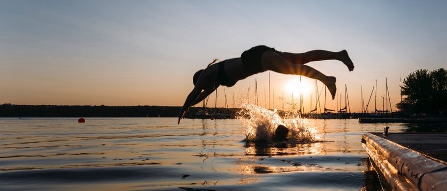 Frau springt bei Sonnenuntergang vom Steg in den See