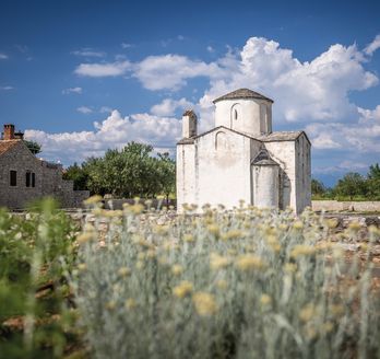 Eine historische Kirche in Nin, Kroatien, umgeben von trockener Vegetation.