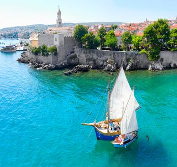 Ein Segelboot im Hafen von Krk, Kroatien, mit der Altstadt im Hintergrund.