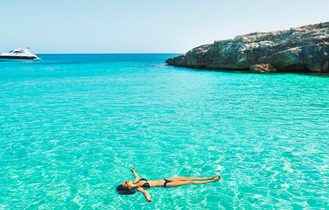 Ein Strand mit türkisfarbenem Wasser und einer Person im Meer.