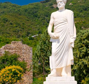 Weiße große Statue vor kleiner Gedenkstätte und Wald im Hintergrund.