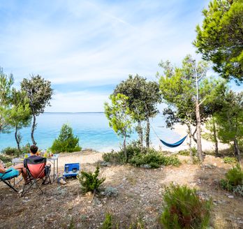 Campingplatz in Kroatien mit Zelten und Campervans am Wasser, umgeben von Bäumen.