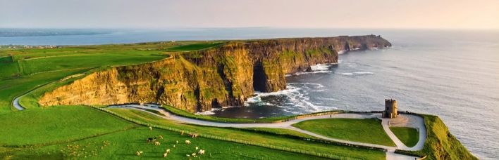 Straße an Klippe mit Ruine und hellgrüner Wiese in Irland
