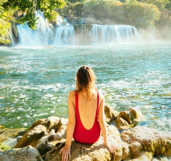 Eine Person sitzt an einem Wasserfall und blickt auf das Wasser.
