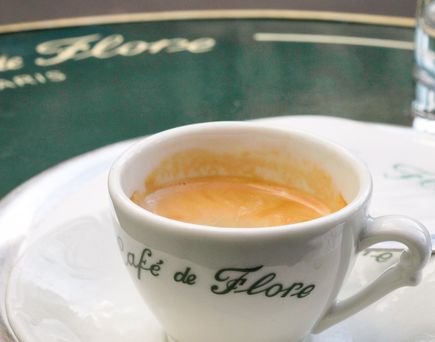 Eine Tasse Kaffee auf einem Tisch in einem Café. Die Tasse ist weiß, mit einem hellbraunen Kaffee.