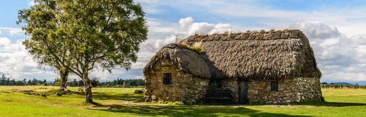 Blick auf ein Steinhaus in Culloden Battlefield, sehr ruhig gelegen und nur umgeben von einem Baum und einer saftigen Wiese.