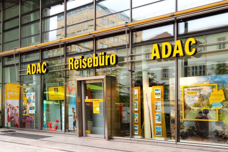 ADAC Reisebüro mit gläserner Fassade und gelber Beschriftung in einer Innenstadtlage, Schaufenster mit Urlaubsangeboten.