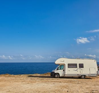 Ein Wohnmobil steht an einer trockenen Küste, das Meer und strahlend blauer Himmel im Hintergrund.