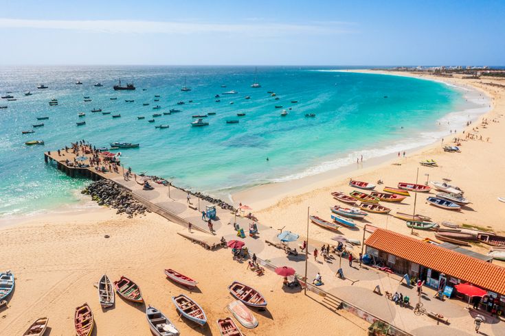 Pier und Boote am Strand vor türkisem Wasser am Strand von Santa Maria, Sal