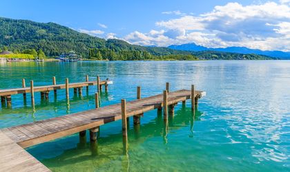 Zwei Holzstege ragen in das türkisblaue Wasser des Wörthersees in Österreich, umgeben von grünen Hügeln.