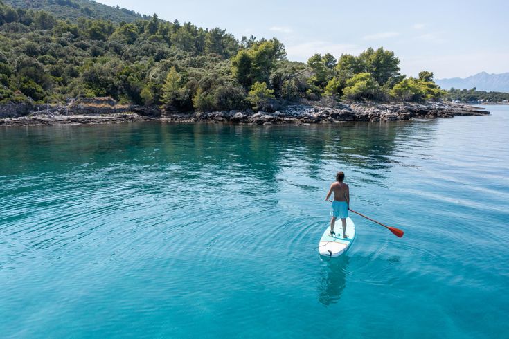 Eine Person steht auf einem Stand-Up-Paddleboard auf klarem, blauem Wasser.